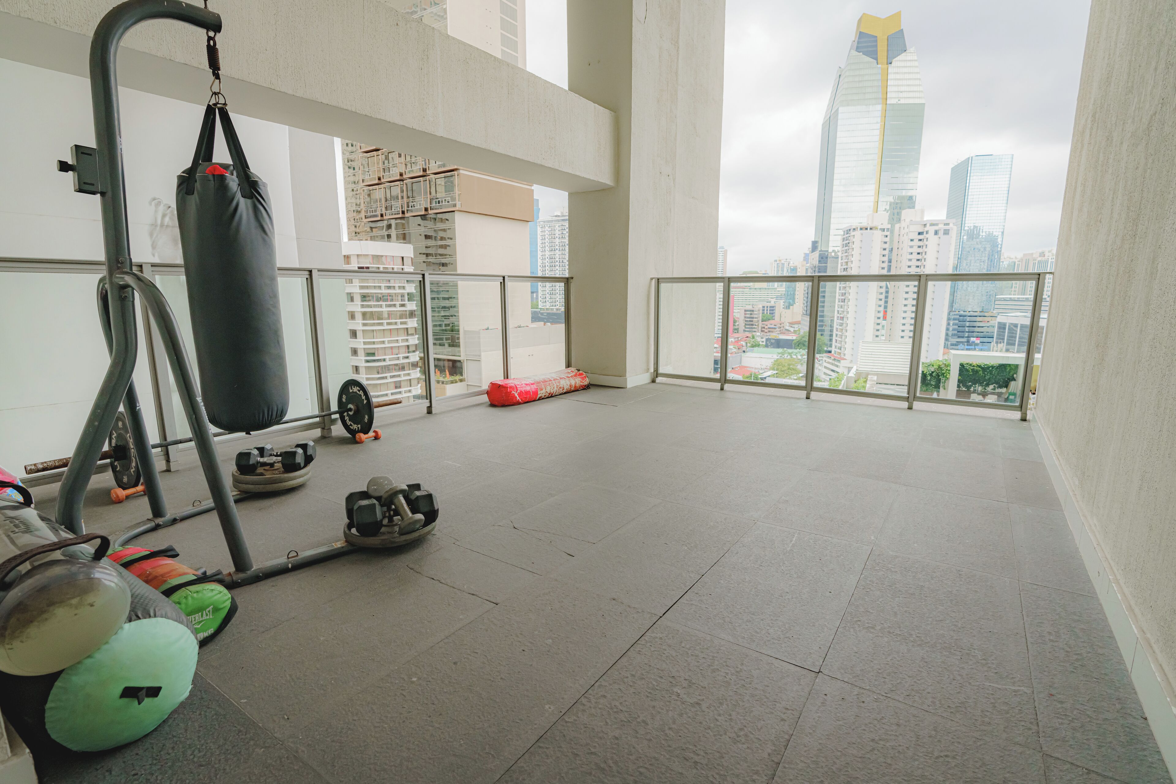 A spacious balcony with gym equipment, a punching bag, and a view of city buildings.