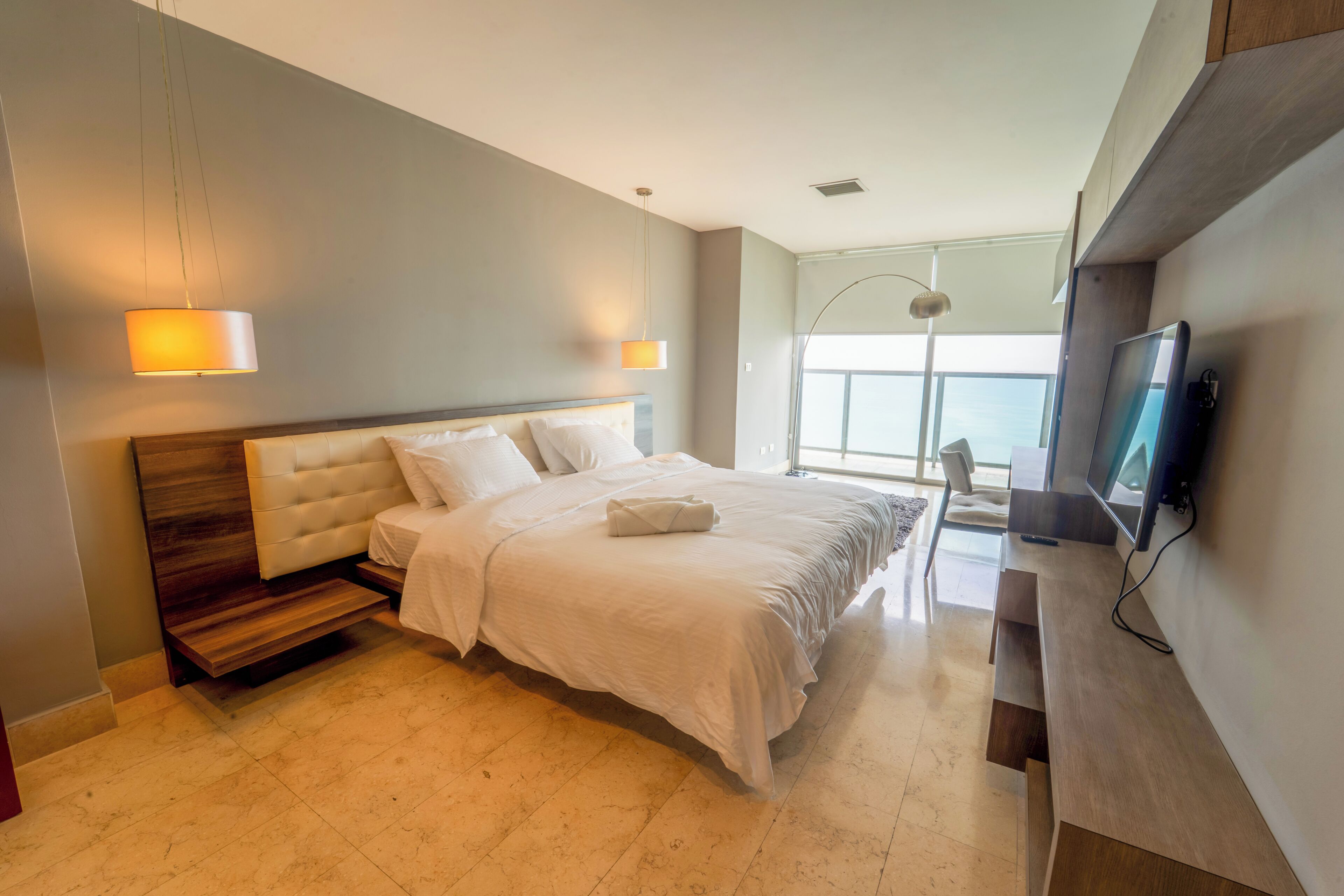 A modern bedroom with a large bed, a desk, and a TV.