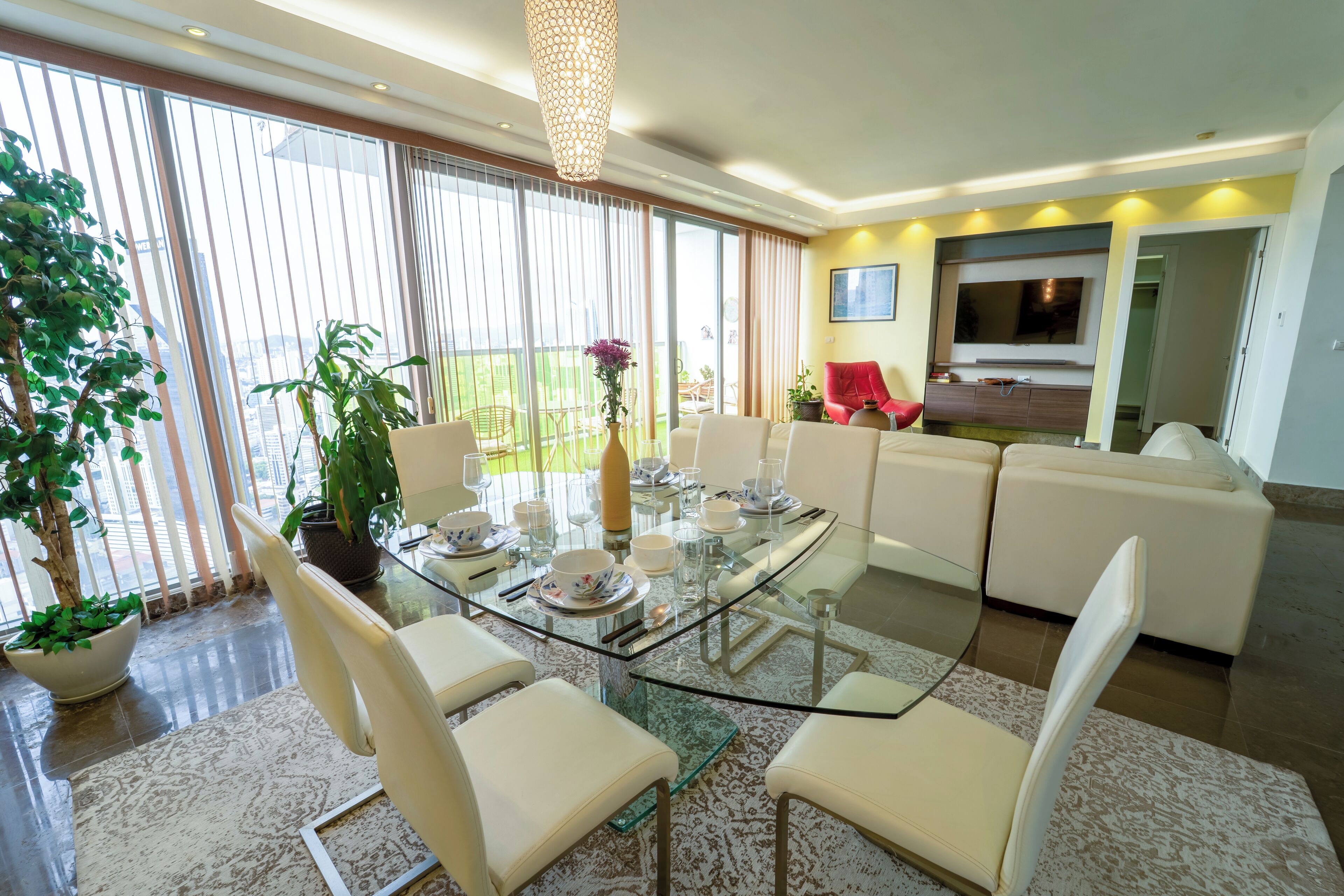 Una sala de estar moderna con una mesa de comedor de vidrio, sillas blancas, un sofá rojo y un televisor montado en la pared.