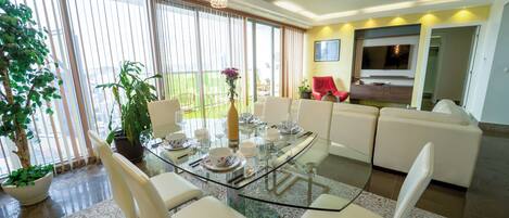 Una sala de estar moderna con una mesa de comedor de vidrio, sillas blancas, un sofá rojo y un televisor montado en la pared.