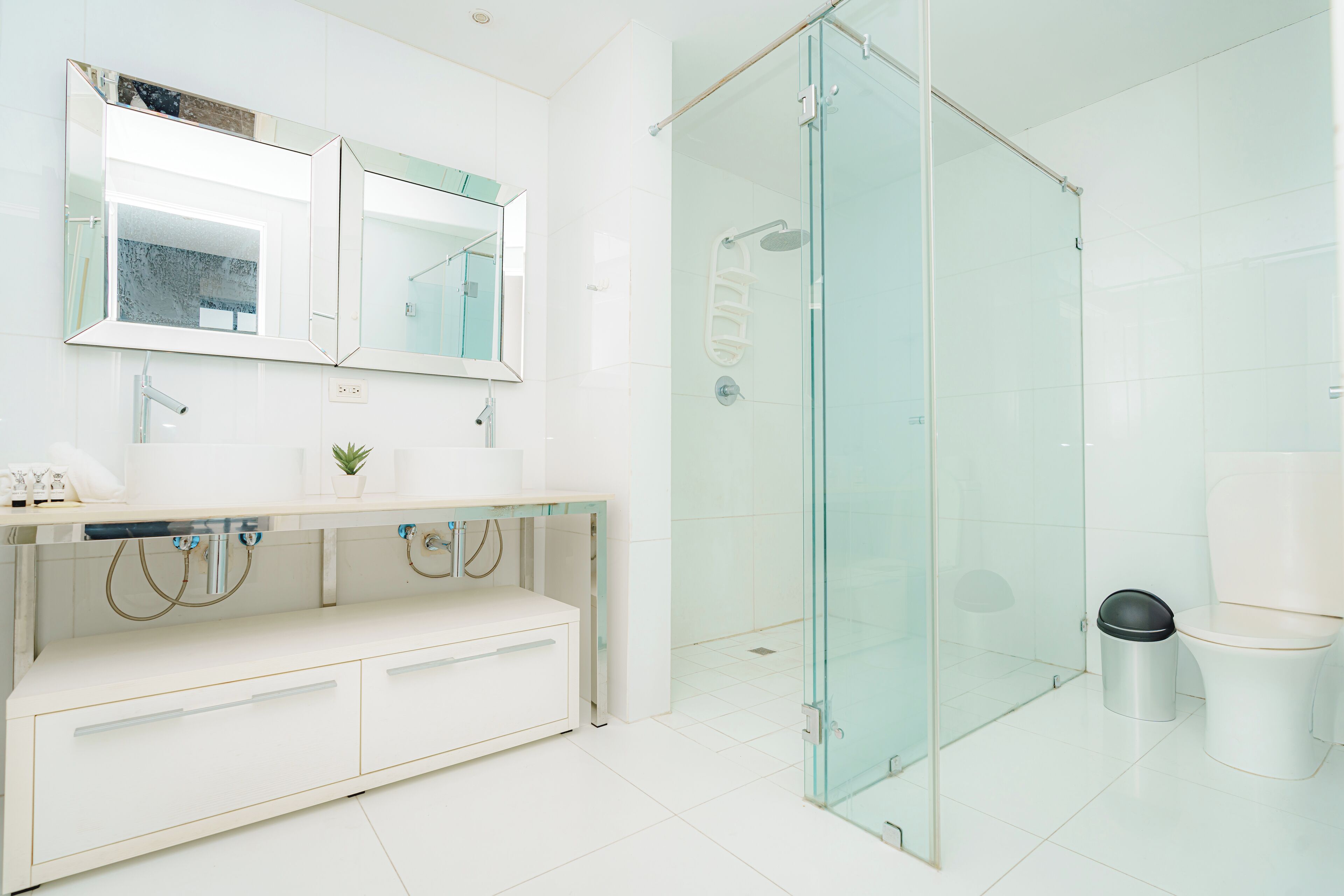 Un baño moderno con cabina de ducha de vidrio, un lavamanos blanco con un espejo encima y un inodoro.