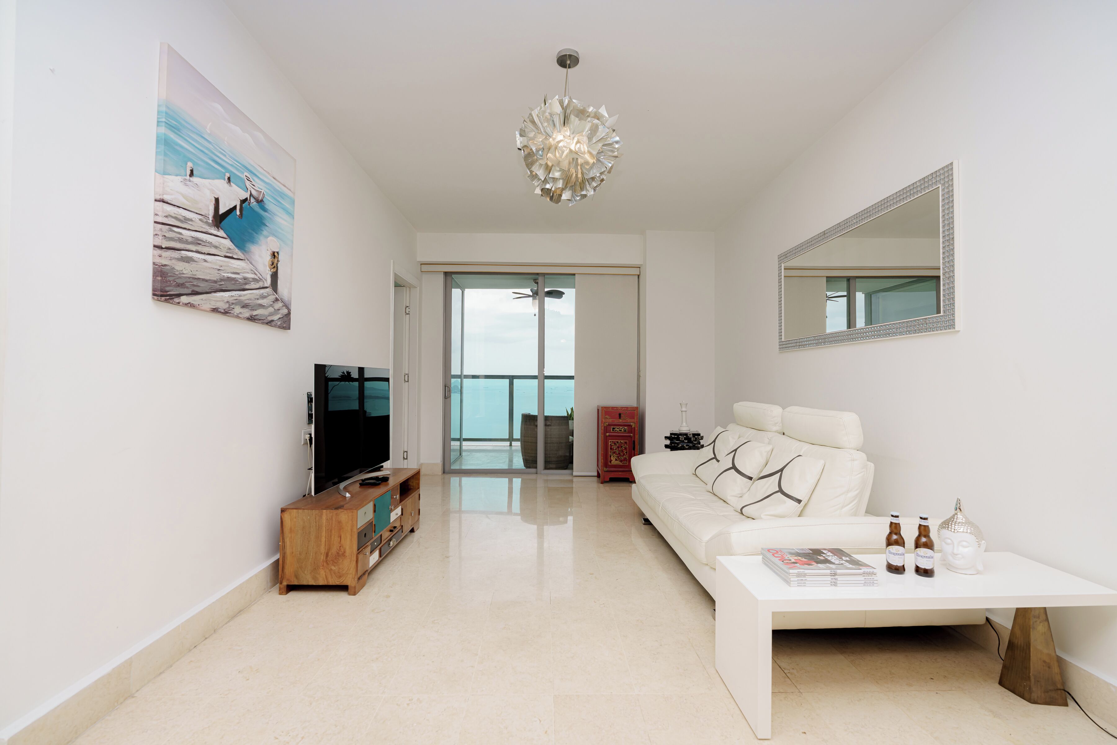 A modern living room with a white sofa, a coffee table, a TV, and a painting on the wall.