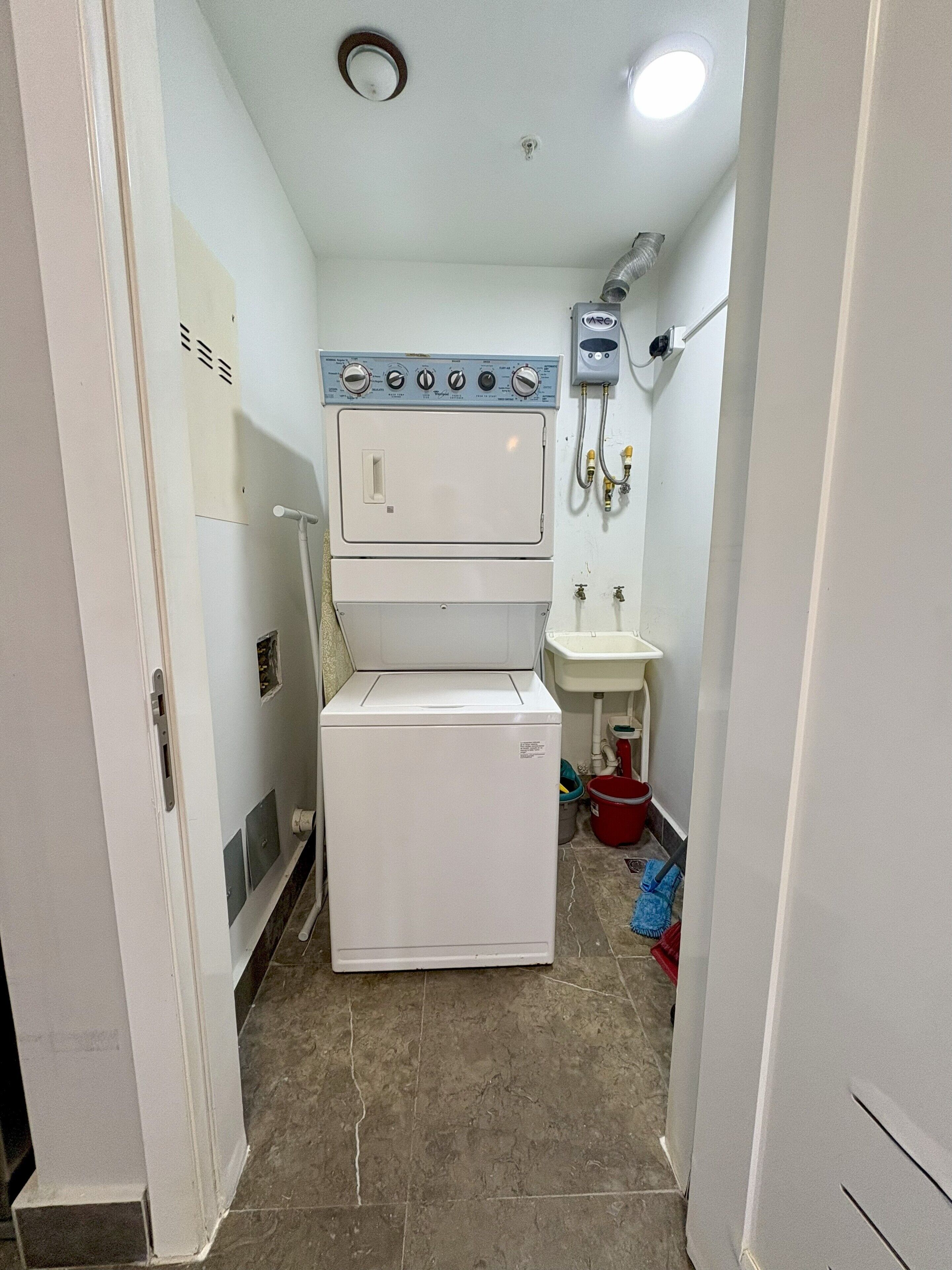 Un lavadero pequeño con lavadora y secadora apiladas, un lavabo y una conexión para manguera.