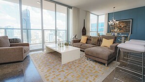 Un salon moderne avec une grande fenêtre, une table basse blanche, un canapé marron et un tabouret de bar.