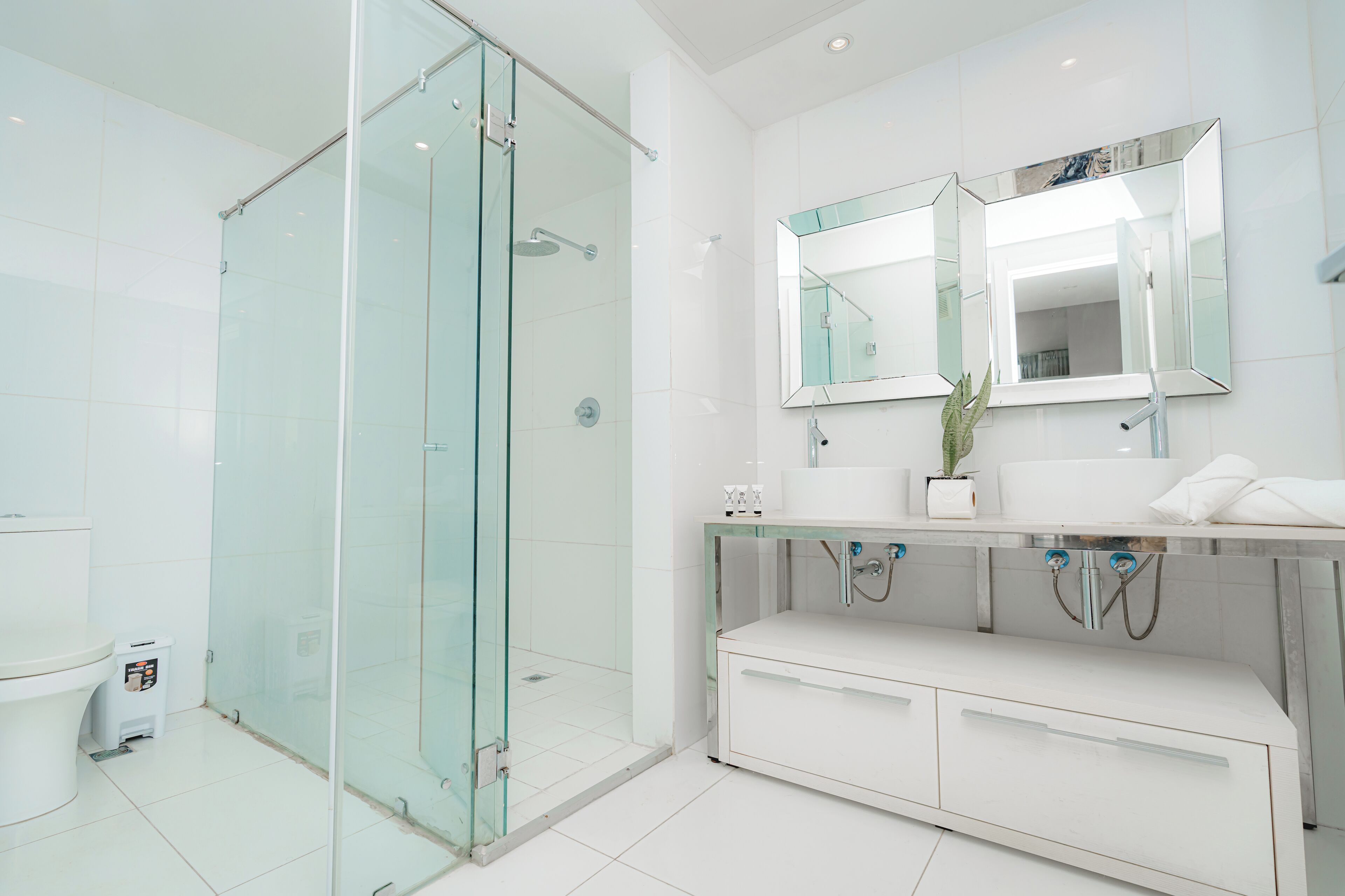 Un baño moderno con ducha de vidrio, un espejo grande y un tocador blanco con cajones.