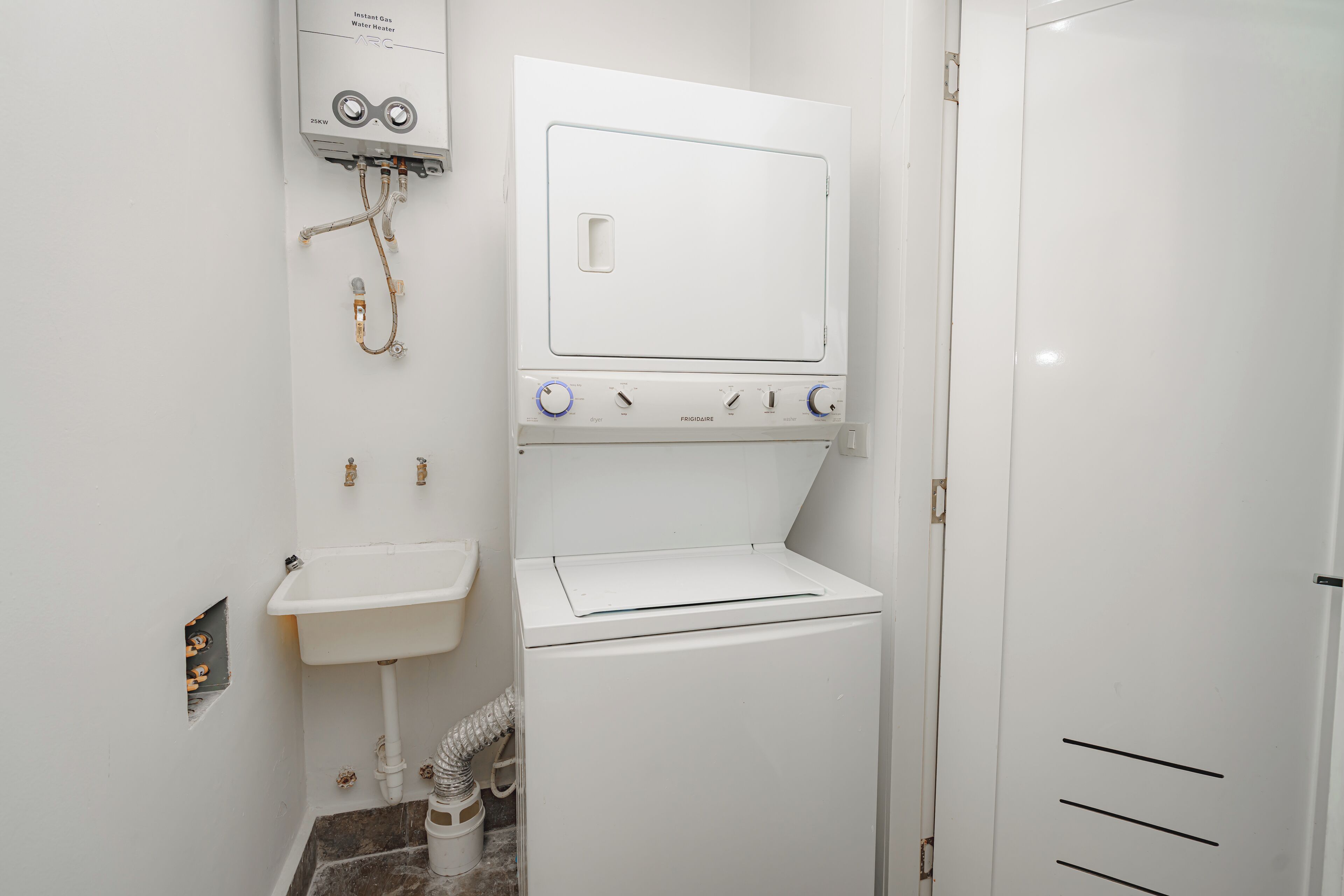 A compact laundry room with a washing machine, a sink, and a door.