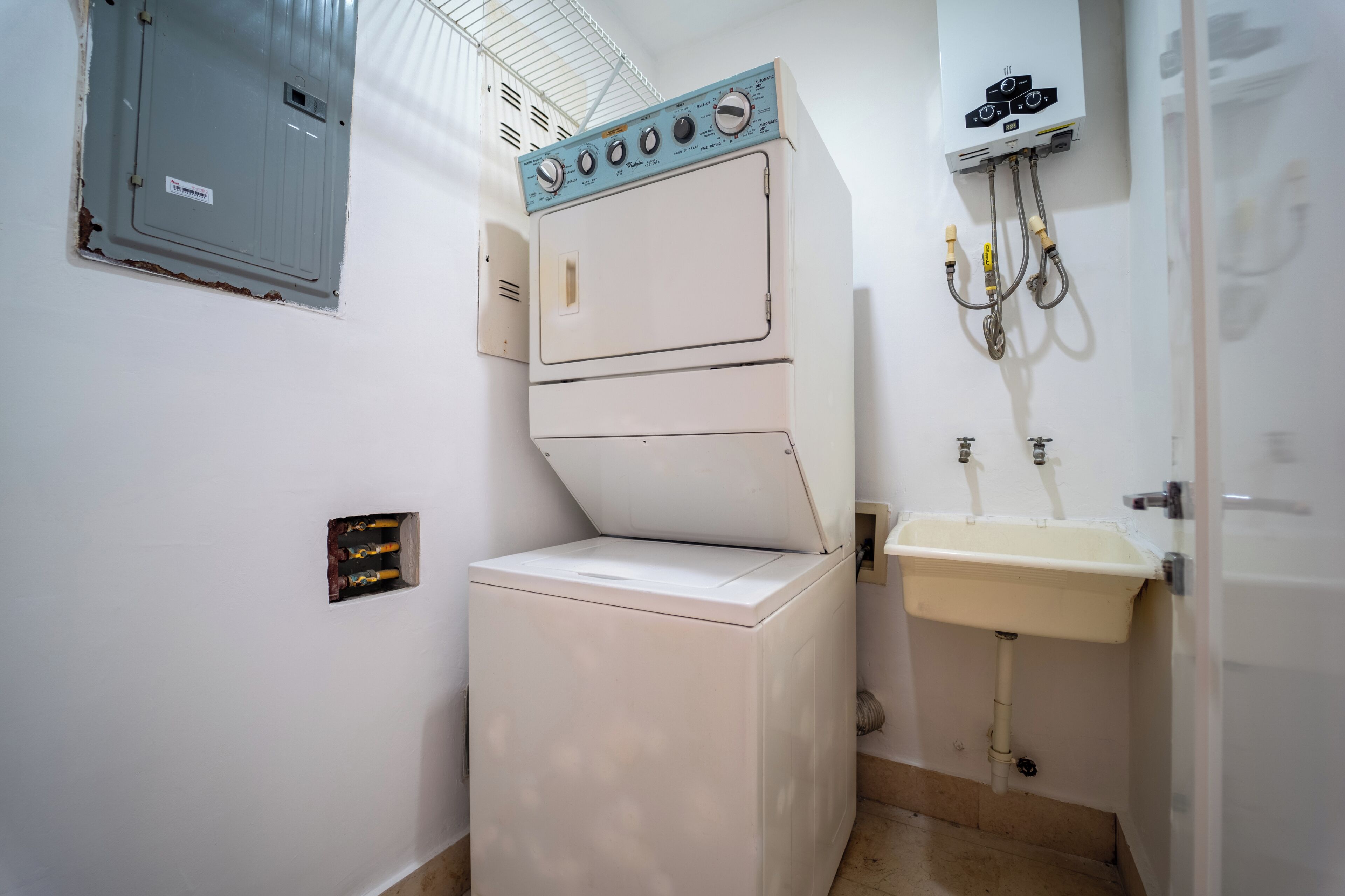 A laundry room with a stacked washer and dryer, a utility meter, and a sink.