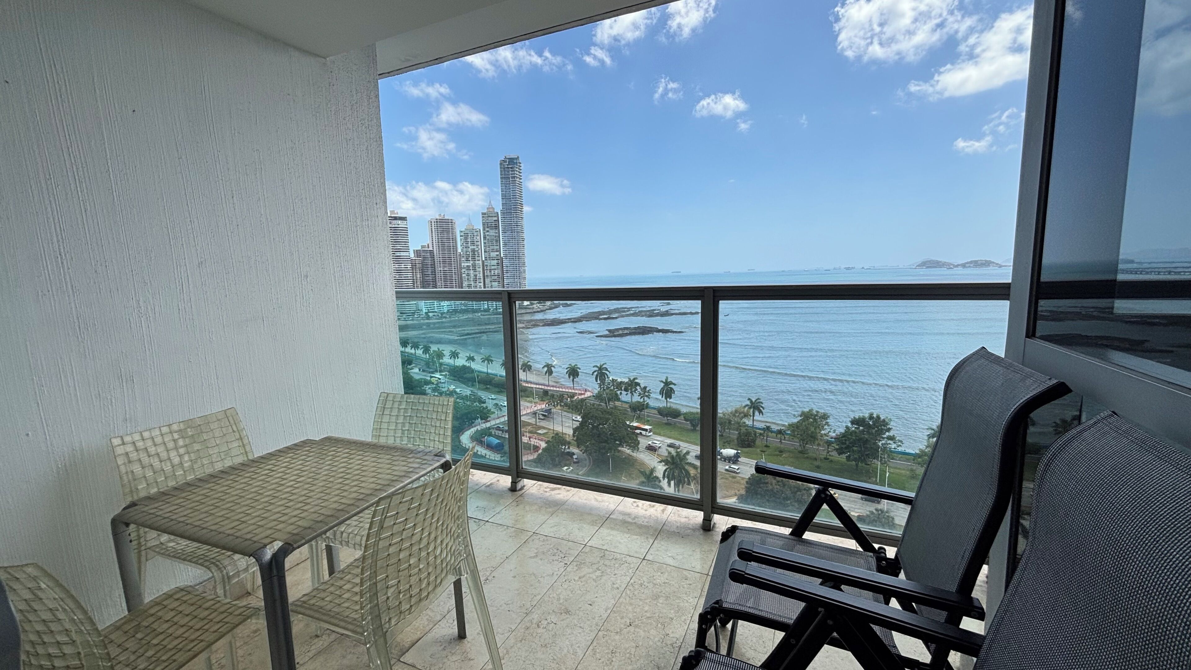 A balcony with a view of the ocean and city skyline, furnished with a table and chairs.