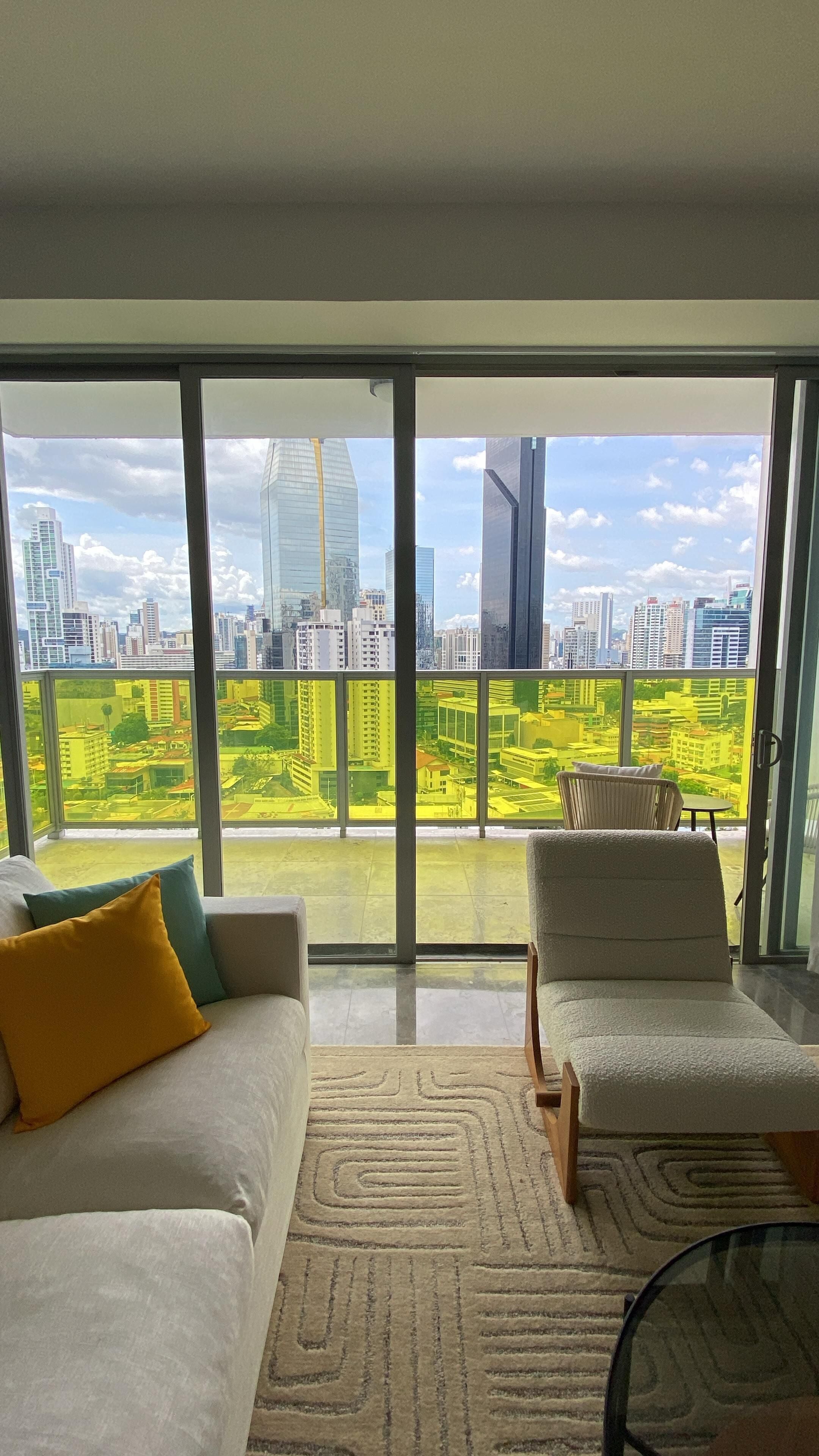 A modern living room with a large sliding glass door leading to a balcony with a city view.