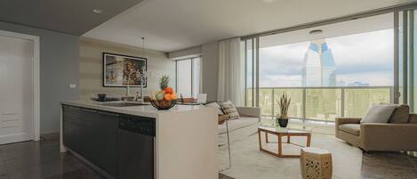 A spacious living area with a kitchen island, a sofa, a coffee table, and a view of a cityscape.