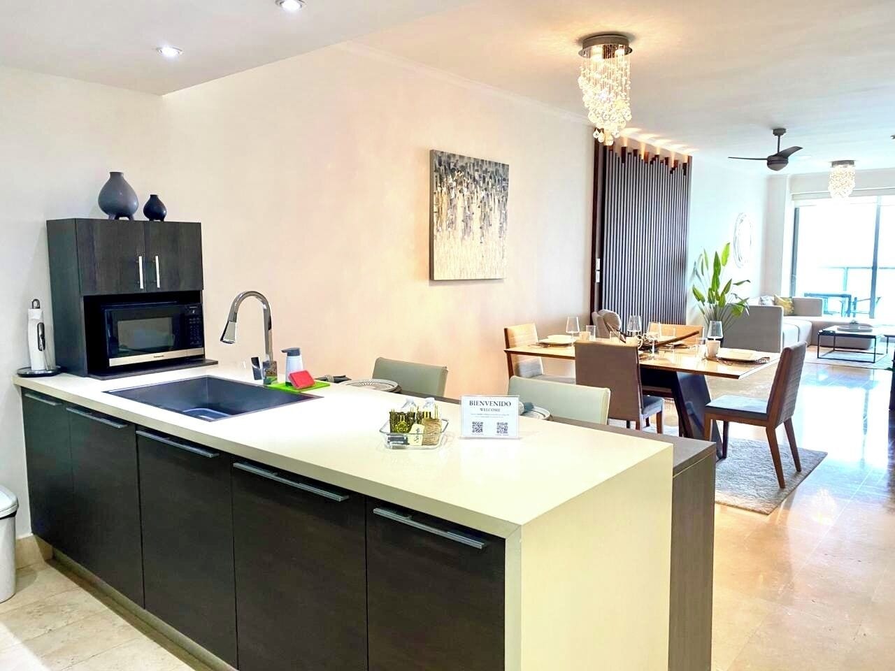 A modern kitchen with a central island, a dining area with a chandelier, and a living space with a view.