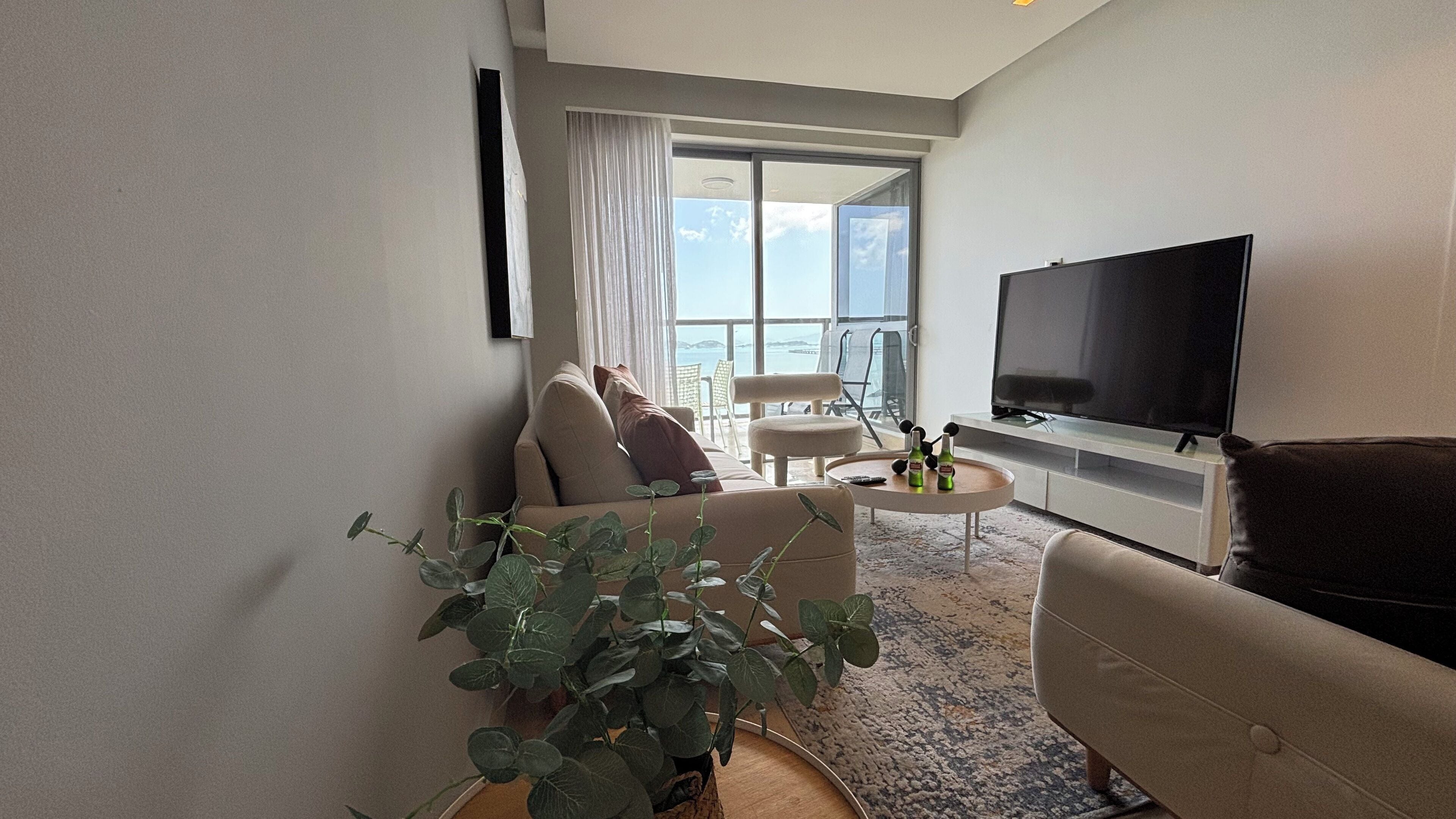 Et moderne hotelværelse med et stort fladskærms-TV, en sofa, et sofabord og en potteplante.