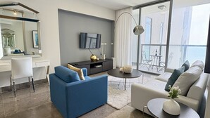Un salon moderne avec un canapé bleu, un canapé blanc, un bureau et une grande fenêtre avec des rideaux.