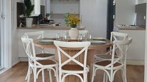 A dining area with a round table set for four, surrounded by white chairs with woven seats. A vase with yellow flowers is placed in the center. - Capel Sound Hideaway (Capel Sound)