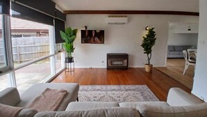 A living room with a fireplace, two potted plants, and a large window. - Capel Sound Hideaway (Capel Sound)