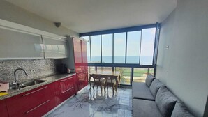 Eine moderne Küche mit Marmorboden, roten Schränken und Meerblick durch große Fenster.