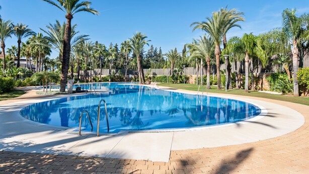 A circular swimming pool surrounded by palm trees and a brick walkway. - Stylish Apartment With Pool in Marbella - Ref M51 (Marbella)