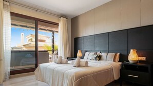 A modern bedroom with a large bed, a dark headboard, and a balcony with a view of buildings. - Stylish Apartment With Pool in Marbella - Ref M51 (Marbella)
