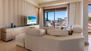 A modern living room with a large flat-screen TV, a white leather sofa, and a dining area with a table and chairs. - Stylish Apartment With Pool in Marbella - Ref M51 (Marbella)