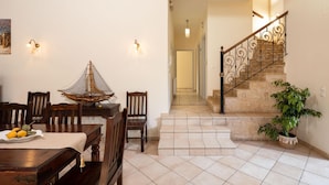 A dining area with a wooden table and chairs, a decorative chair, a small table with fruit, and a potted plant near a staircase. - Villa Lefki Limni Retreat 300m From Beach (Corfu)