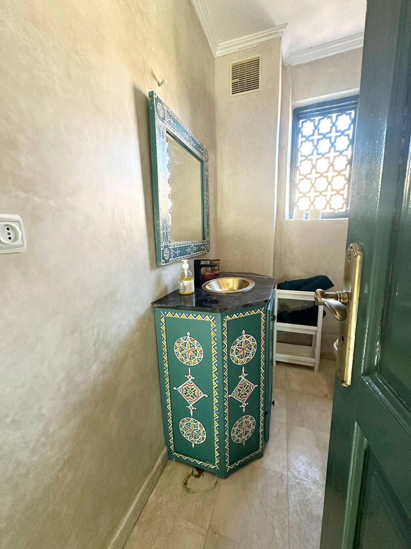 A bathroom with a green cabinet, a sink, a mirror, and a window with a decorative grille.