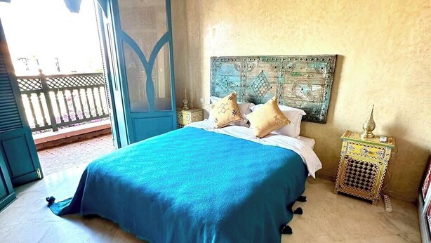 A bedroom with a bed, a nightstand, a decorative headboard, and a view of the outside balcony. - Vacation Riad with private pool 3 CH Hivernage (Marrakech)
