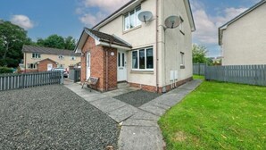 Ein zweistöckiges Wohnhaus mit Satellitenschüsseln, einem kleinen Anbau aus Backsteinen und einem Schotterweg.