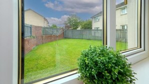 Blick auf einen Garten mit grünem Rasen, einer Ziegelmauer und einem Metallzaun.