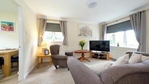 Ein Wohnzimmer mit einer Couch, einem Fernseher, einem kleinen Tisch mit einer Lampe und einem Sessel.