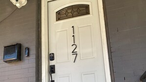 Une porte blanche portant le numéro 127, une boîte aux lettres et une caméra de surveillance fixée au mur.