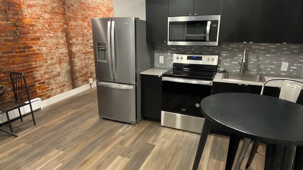 Une cuisine moderne avec un mur en briques, des appareils électroménagers en acier inoxydable et un plancher en bois.
