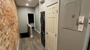 Un couloir avec un mur en briques, un lave-linge et une porte dotée d’un interrupteur.