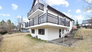 Ett tvåvåningshus med en balkong, en ytterdörr och en liten trädgård framför huset.