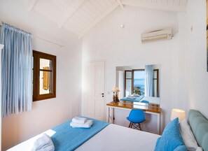 A hotel room with a bed, a desk, a chair, a mirror, and a view of the sea. - Villa Ostria - Two Bedroom Villa, Sleeps 4 (Lefkada)
