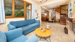 A spacious living area with a blue sofa, a round wooden coffee table, and a dining area with a table and chairs. - Villa Pelagos Kyma - Two Bedroom Villa, Sleeps 4 (Lefkada)