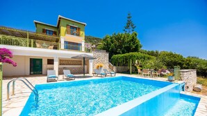 A swimming pool with lounge chairs, a stone wall, and a building with a balcony. - Villa Pelagos Kyma - Two Bedroom Villa, Sleeps 4 (Lefkada)