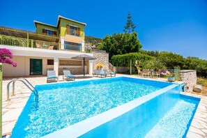 A swimming pool with lounge chairs, a stone wall, and a building with a balcony. - Villa Pelagos Kyma - Two Bedroom Villa, Sleeps 4 (Lefkada)