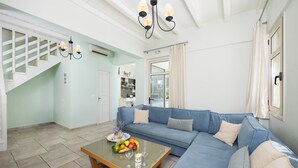 A living room with a blue sofa, a glass coffee table with fruits and wine, a staircase, and a kitchen in the background. - Villa Votsalo - Three Bedroom Villa, Sleeps 6 (Lefkada)