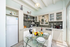A modern kitchen with white cabinetry, a glass dining table, and a variety of kitchen appliances.