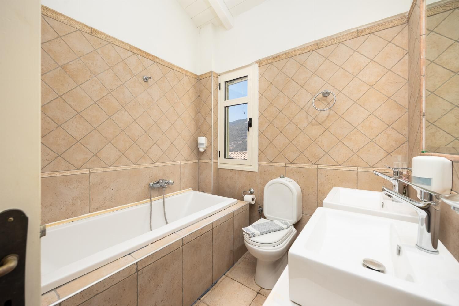 Ein Badezimmer mit Badewanne, Toilette und Waschbecken, mit Fliesenwänden und einem Fenster.