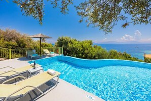Una piscina con vista al mar, rodeada de vegetación y un pabellón.