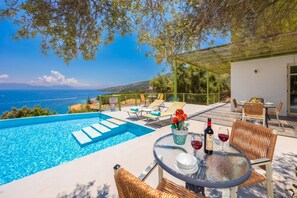 A poolside area with a view of the sea, outdoor seating, and a table set for dining.