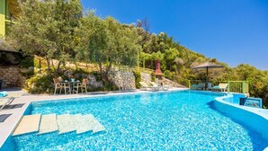 A swimming pool with clear blue water, surrounded by lounge chairs and a stone wall.
