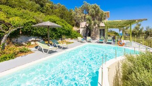 A swimming pool with lounge chairs and a pergola, surrounded by greenery and a stone building. - Villa Anemus - Three Bedroom Villa, Sleeps 6 (Lefkada)