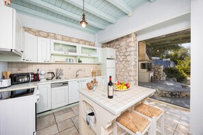 A kitchen with white cabinets, a stone wall, a built-in oven, and a dining area with wicker chairs.