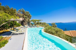 A pool area with lounge chairs and a view of the sea.