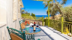 A terrace with a table, chairs, a bottle of wine, and a view of the sea. - Villa Anemus - Three Bedroom Villa, Sleeps 6 (Lefkada)
