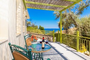 A terrace with a table, chairs, a bottle of wine, and a view of the sea.