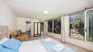 A bedroom with a bed, a sofa, and a wardrobe. There is a bathroom with a shower and a toilet visible through an open door. - Villa Anemus - Three Bedroom Villa, Sleeps 6 (Lefkada)