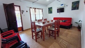 Un área de comedor con una mesa y sillas de madera, un sofá rojo y un televisor montado en la pared.